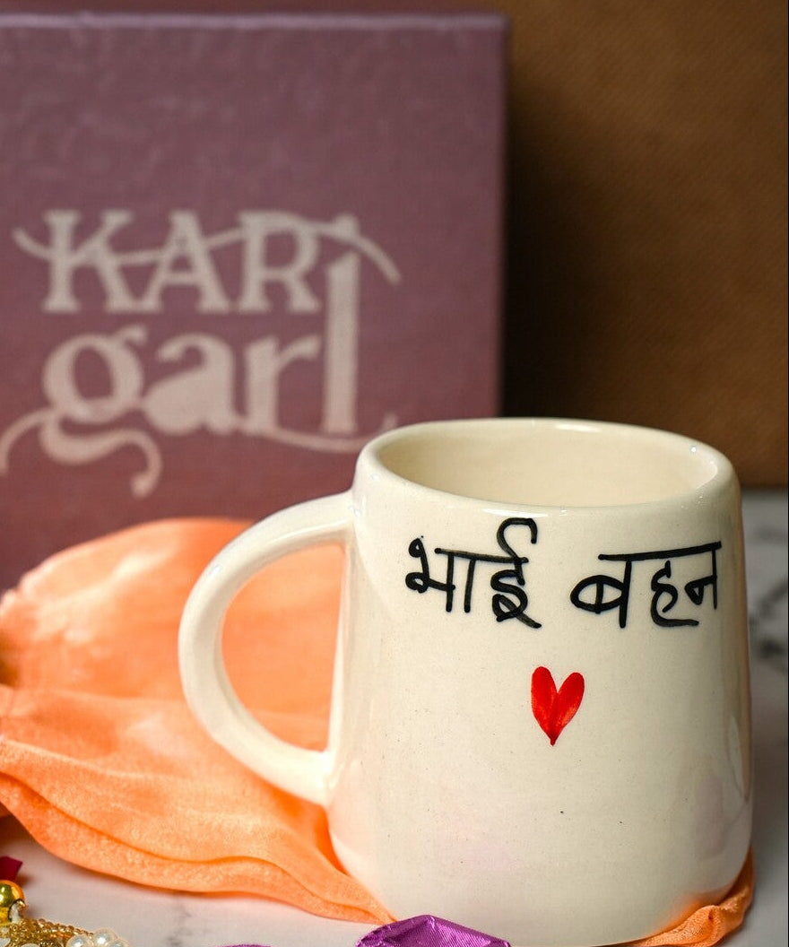 White mug with text, marigold flowers, and decorative items on a marble surface with 'Kari Garl' box in the background.