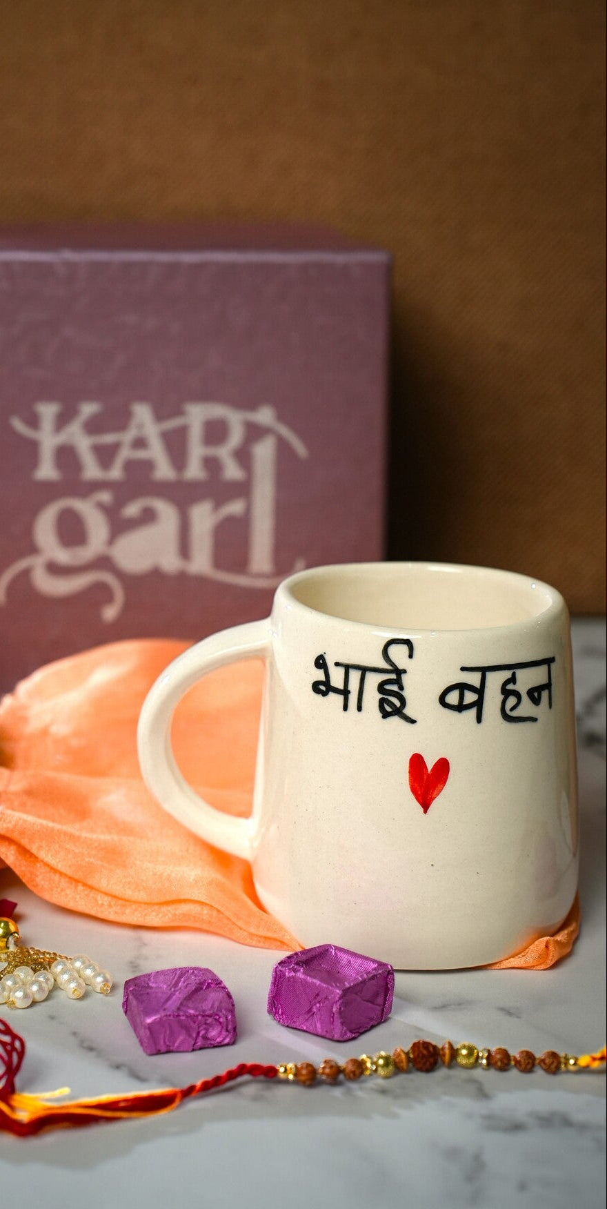 White mug with text, marigold flowers, and decorative items on a marble surface with 'Kari Garl' box in the background.